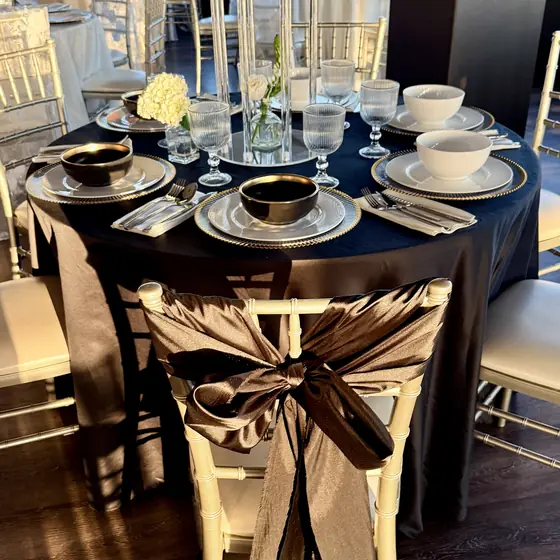 Black satin tablecloth with gold-rim chargers in daylight